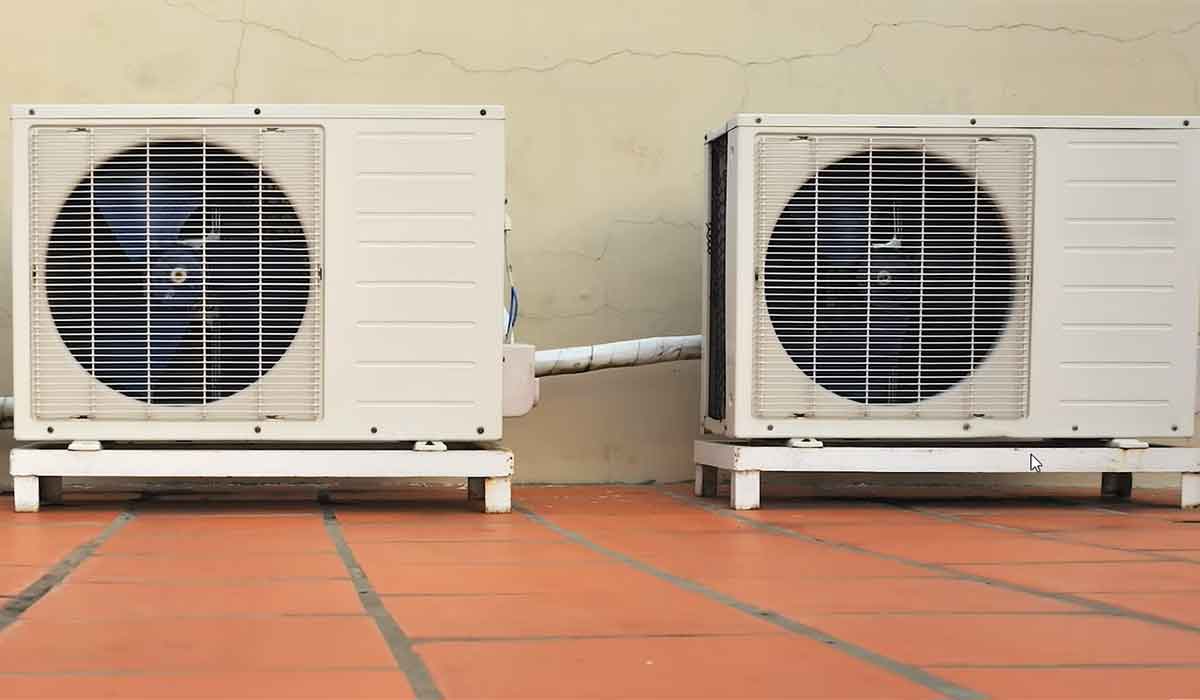 Two outdoor HVAC condenser units installed side by side on a tiled surface against an exterior wall