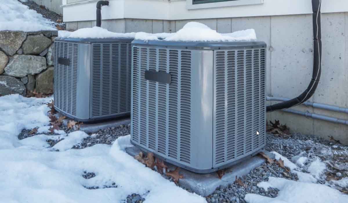 Two outdoor HVAC condensers beside a house with snow on top and around the units in winter