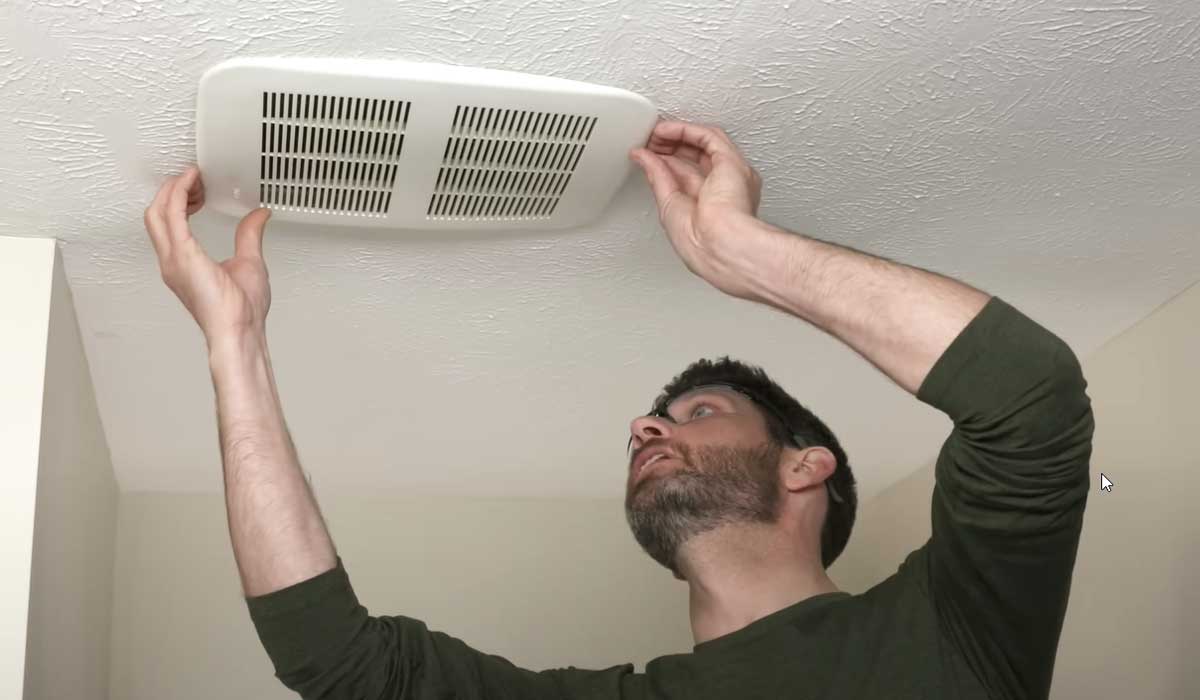 Man removing a ceiling vent cover for cleaning or maintenance