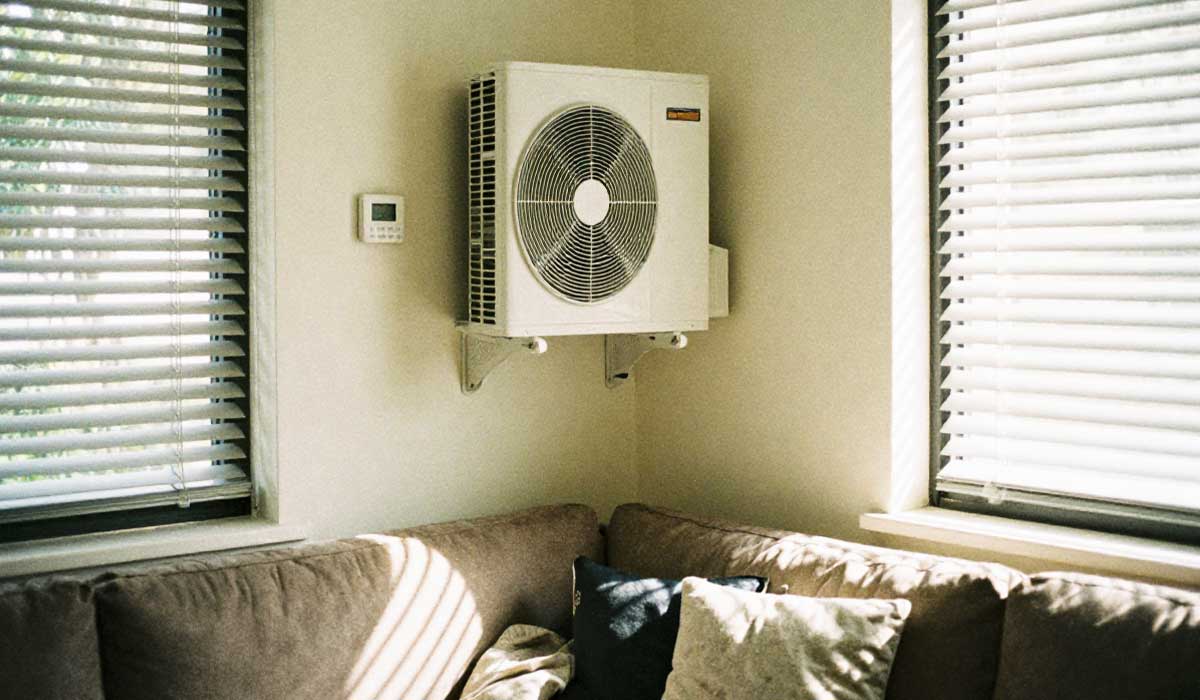 Wall-mounted HVAC unit above a sofa between two windows in a bright room