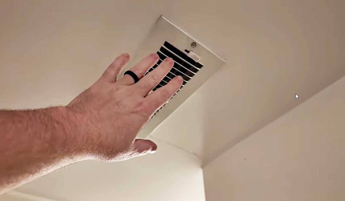 Hand checking airflow from a ceiling air vent in a home