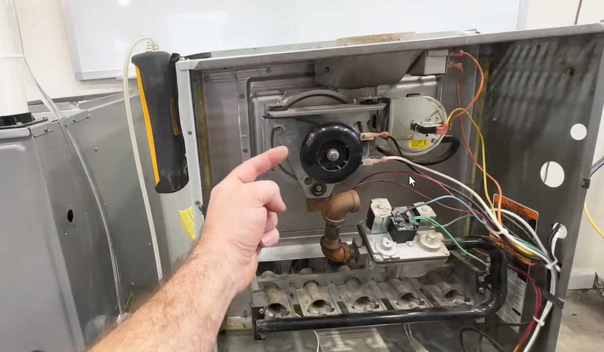 Open furnace interior with a hand pointing to internal components during HVAC inspection