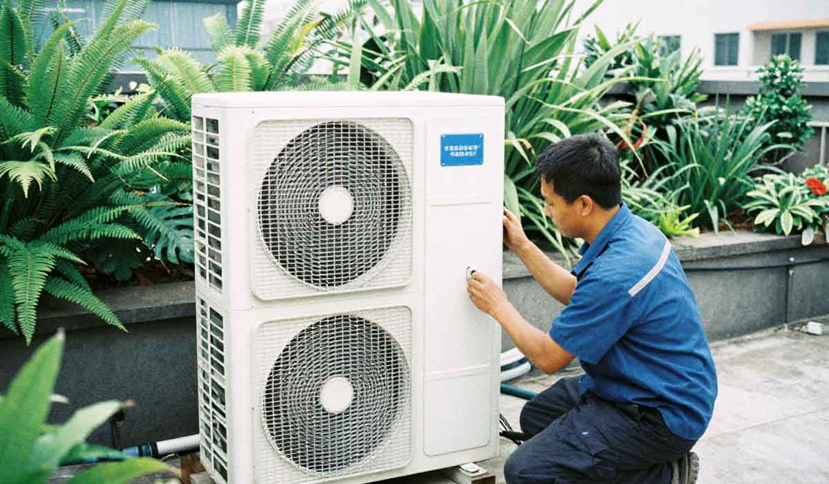 Technician servicing an outdoor HVAC condenser unit beside dense landscaping