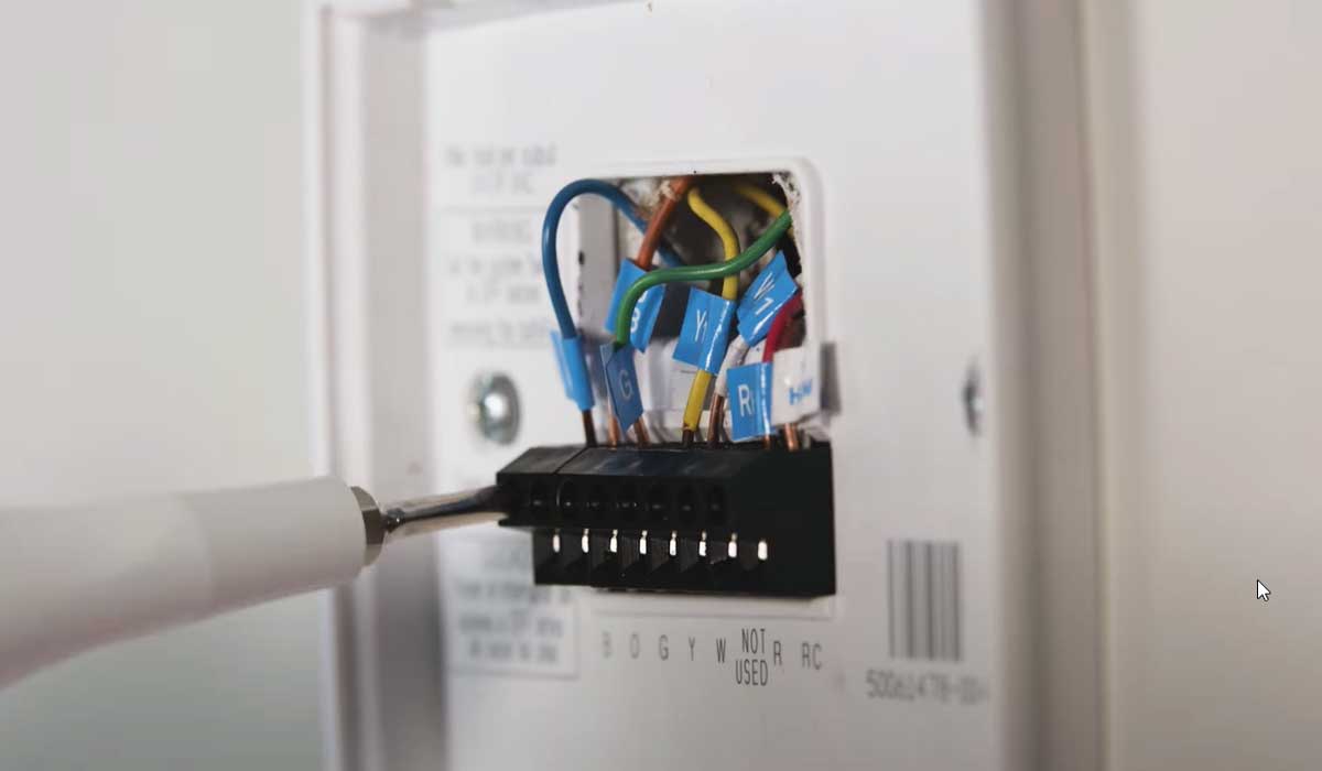 Close-up of thermostat wiring terminals being adjusted with a screwdriver during HVAC setup