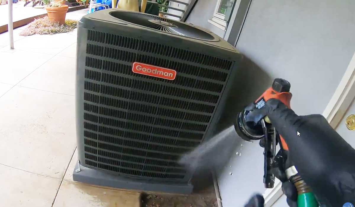 Technician rinsing a Goodman outdoor AC condenser during routine maintenance