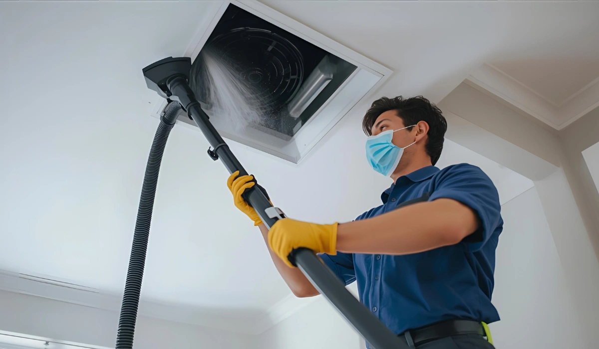 Technician in gloves vacuuming a ceiling vent in a modern home interior during air duct cleaning.