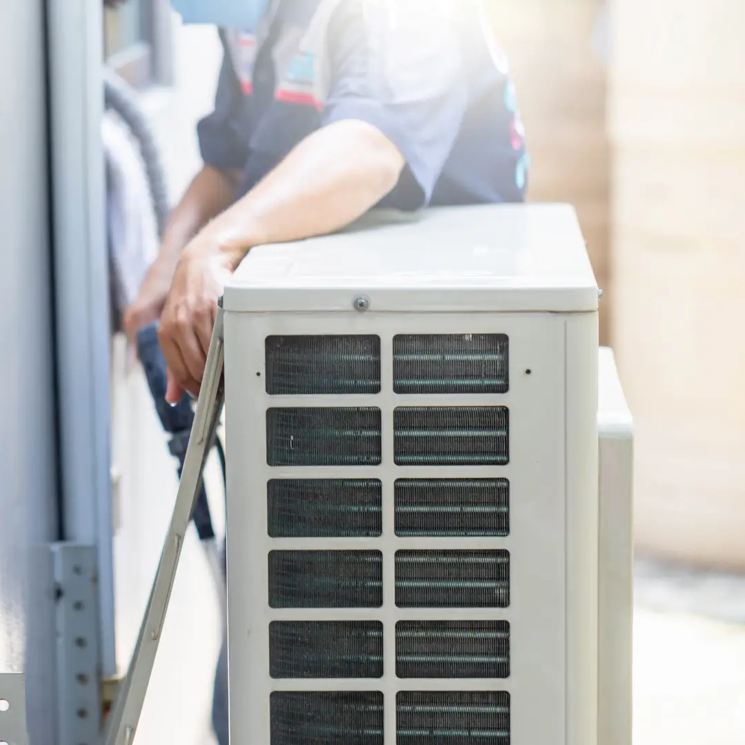 A technician in uniform installing or repairing an outdoor air conditioning unit mounted next to a building.