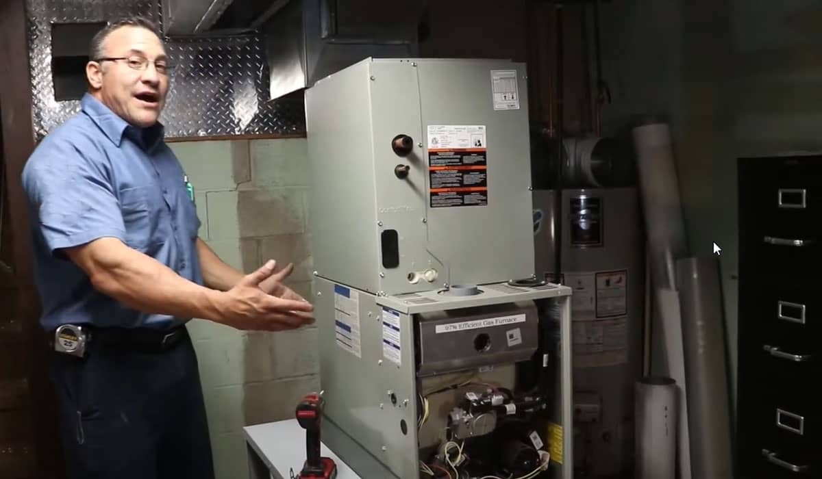HVAC technician standing beside an indoor furnace in a basement utility room during inspection.