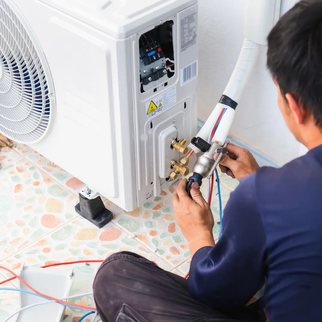 A technician connects pipes and wires while installing or repairing an outdoor AC unit on patterned tiles, highlighting expert HVAC service in Durham, NC.