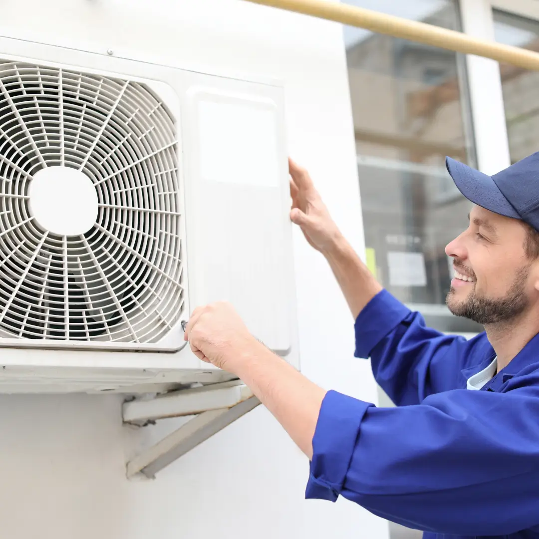 A technician in a blue uniform performs maintenance on a wall-mounted AC unit, representing expert residential HVAC services in North Carolina.
