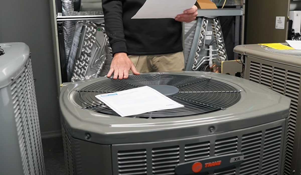 Person reviewing a Trane outdoor AC condenser with paperwork in an HVAC showroom