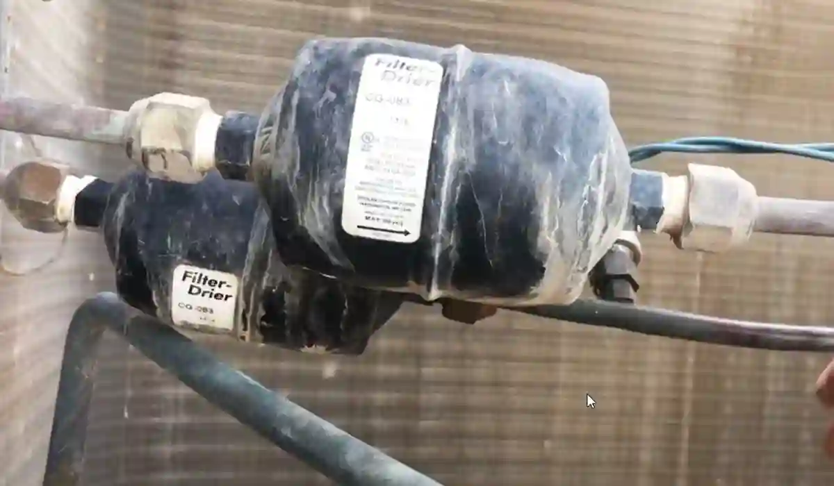 Close-up of HVAC filter drier components installed on refrigerant lines near an outdoor AC unit
