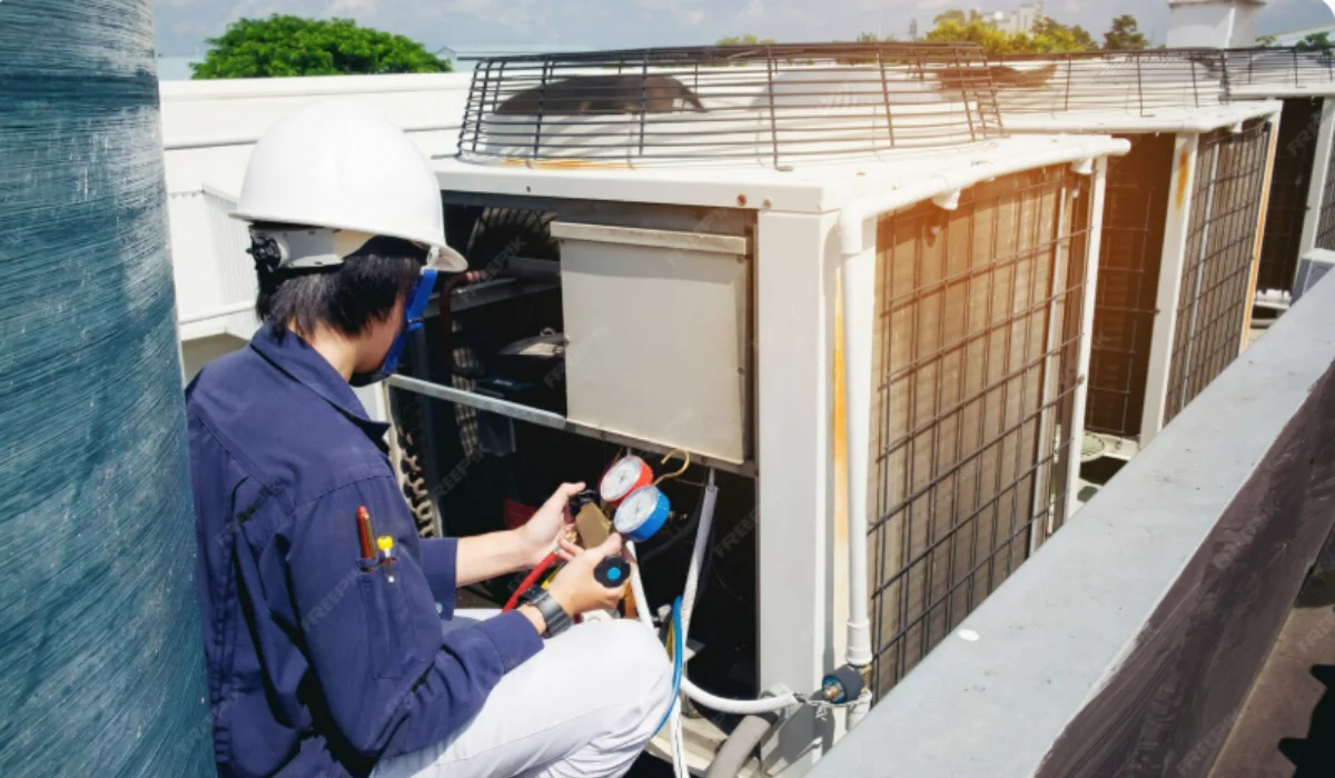 Technician inspecting a rooftop commercial AC unit with pressure gauges during HVAC service