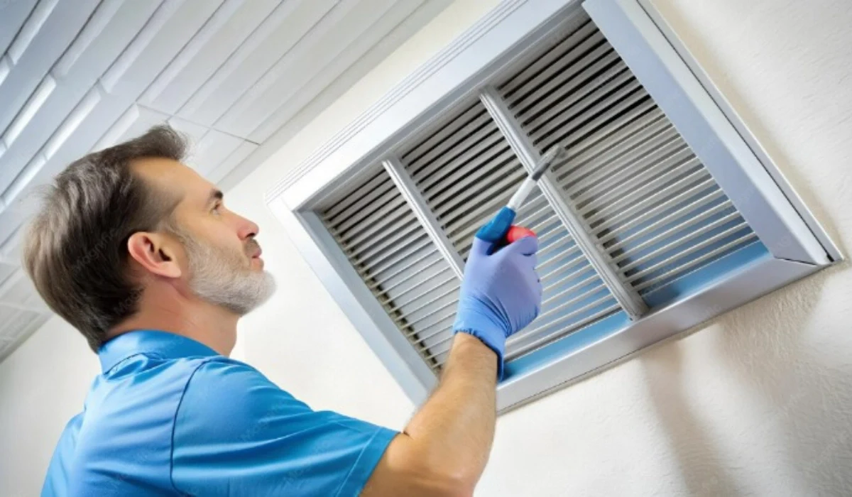 Man using a screwdriver on a wall return vent grille during HVAC vent maintenance.